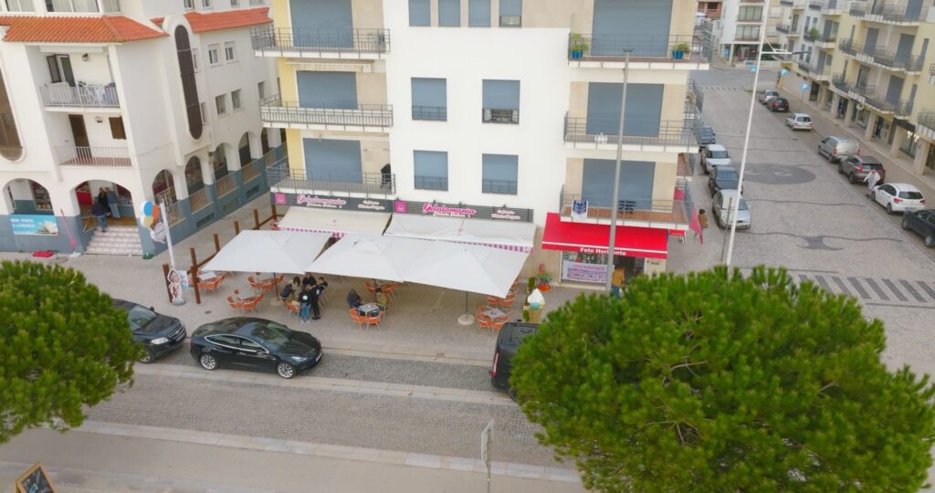 Vista panorâmica da Gelatomania de São Martinho do Porto, com uma visão ampla da rua onde se situa, e das suas mesas convidativas com os clientes a desfrutar dos seus gelados.